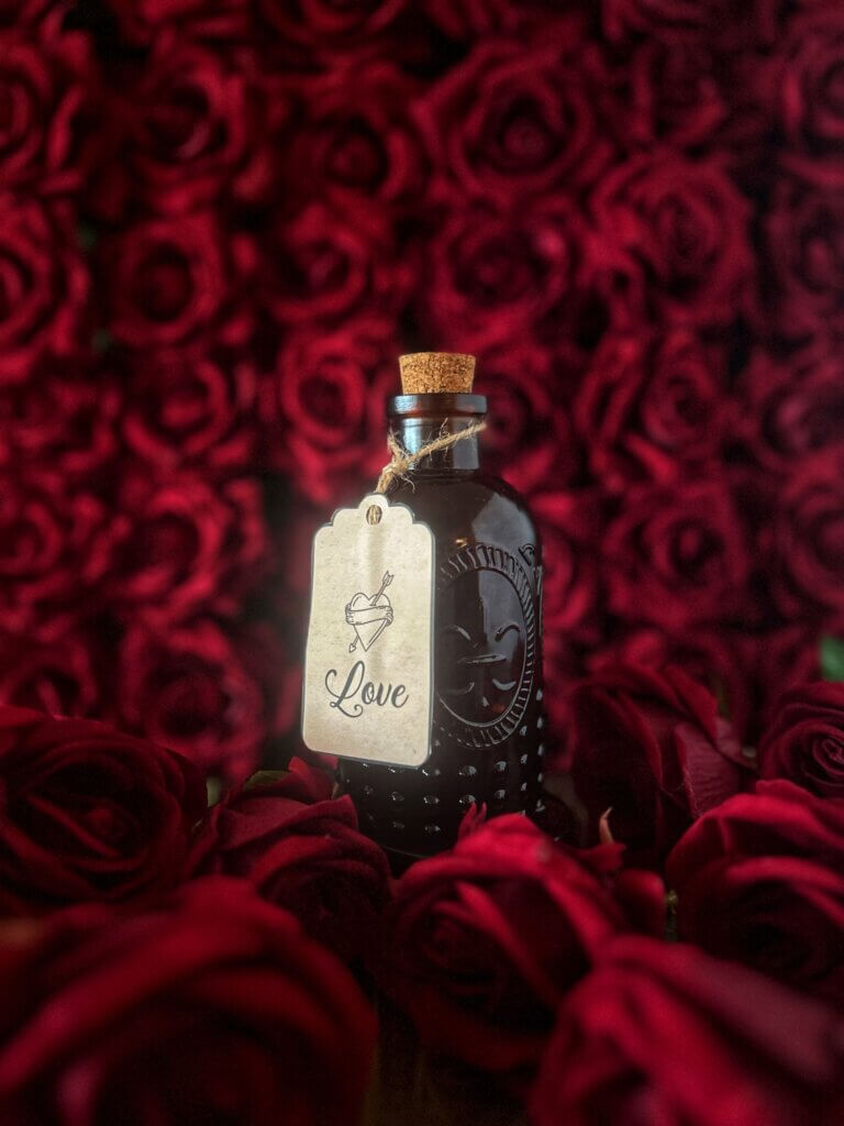 Apothecary bottle with a label saying bitters for love stands surrounded by red roses
