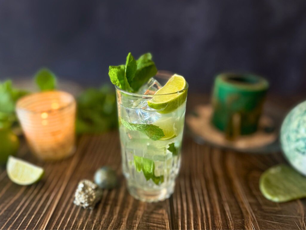 A mojito mocktail in a cut crystal glass surrounded by candles and greencrystals believed to enhance luck