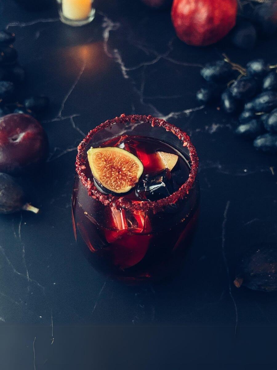 A glass of non-alcoholic sangria surrounded by assorted fruit garnishes like black grapes, plums and pomegranates