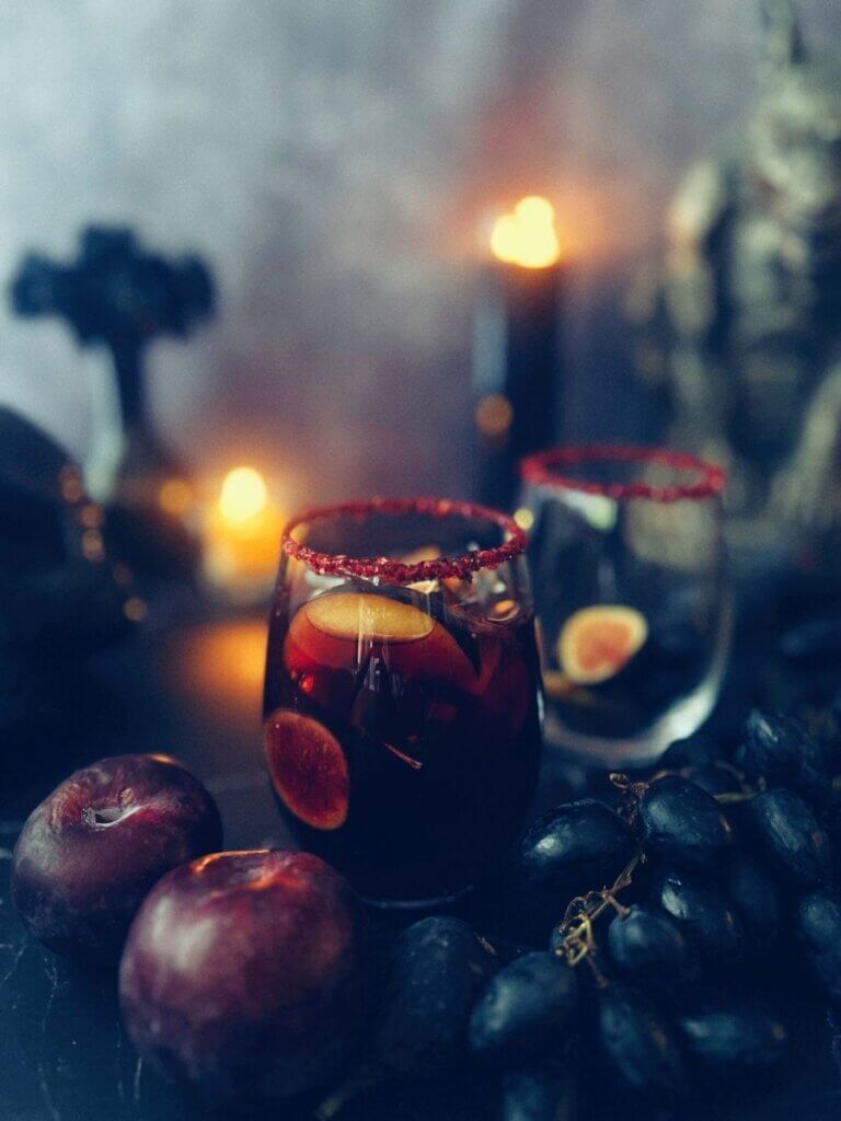 A glasses of Halloween sangria surrounded by assorted fruit garnishes and spooky Halloween decor